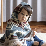 toddler sitting down wearing a light blue poncho with the hood on 