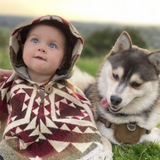 baby wearing a poncho with the hood on next to a husky puppy