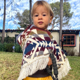 toddler wearing a colorful poncho looking at the. camera with a house in the background