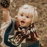 Little girl wearing a rainbow color poncho grabbing a pinecone 