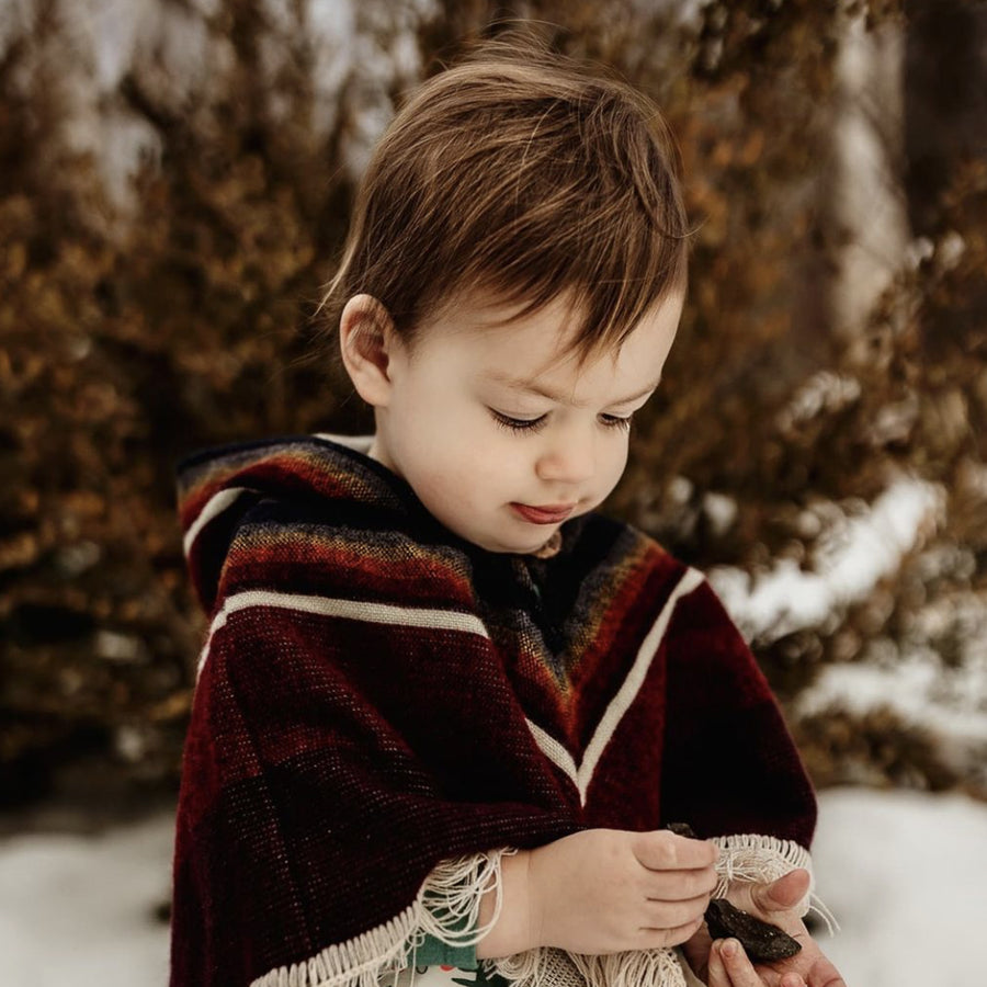 toddler looking down playing with rocks in the snow wearing a siena color with white v shape patterns 