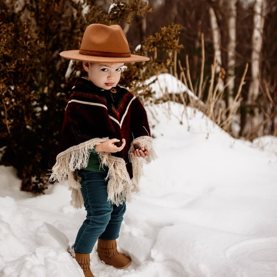 toddler playing with rocks in the snow wearing a siena color with white v shape patterns and a brown hat